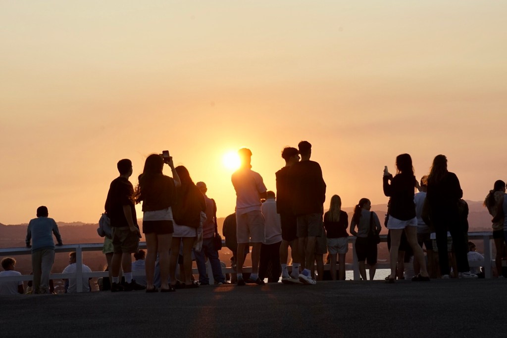 A group of people standing on a cliff, silhouetted against a vibrant sunset, symbolizing the beauty of life’s fleeting moments and the power of shared experiences.